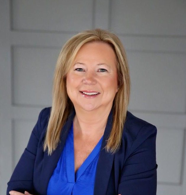 Smiling woman in blue blazer, grey background.